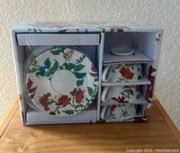 Boxed set of 4 tea cups and saucers with floral pattern visible, showing side and front of cups stacked next to matching saucers.