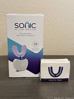Box of Sonic Glow Brush fully automatic ultra-sonic toothbrush next to box with additional mouth tray