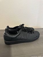 Side view of vintage Adidas black shell toe sneaker showing black leather upper with Adidas stripes and black rubber sole.