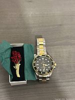 Tevise wristwatch and red flower brooch displayed in a small box with green tissue paper.