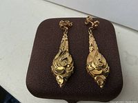 Front view of pair of gold drop earrings on brown display pad