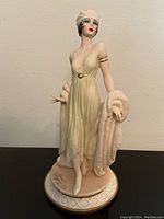 Front view of porcelain figurine showing the woman in pale green dress with white hat and fur stole, signed base visible.