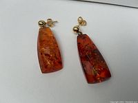 Pair of earrings on white background showing amber dangles and gold posts
