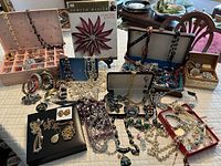 Overview of jewelry lot on table showing boxes, necklaces, brooches, book and assorted pieces