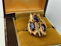 Front view of the brutalist style ring with three marquise-cut amethysts set in 14k yellow gold, displayed in velvet-lined box