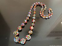Full view of the entire 32-inch strand showing the colorful and detailed Murano glass millefiori beads arranged in a curved shape on a dark surface.