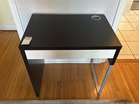 Photo showing top and front view of small black Ikea desk with metal drawer panel and cable hole.