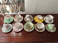 All ten teacup and saucer sets arranged in two rows on wooden table