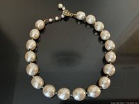 Full view of necklace laid flat showing strand of large faux pearls and clasp.