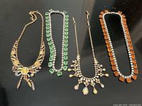 Full view of the set of four unique vintage rhinestone necklaces arranged in a single row on a black background.