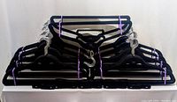 Photo shows 100 black felt hangers bundled in groups of ten with purple bands, along with 8 pant attachments in the center, displayed on a white surface.