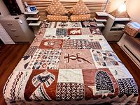 Full view of the queen bed with the African hand-painted patchwork bedspread laid out, showing earth tone motifs of fish, birds, and animals