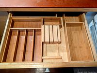 Photo showing bamboo drawer organizers and dividers arranged inside a drawer with varied section sizes and one large open compartment.