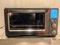 Front view of Breville Smart Oven Air showing digital display illuminated at 425°F and 15 min timer, analog control knobs, and interior with oven rack inside.