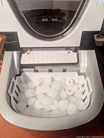 Top view opened showing removable white plastic basket filled with bullet-shaped ice cubes inside the ice maker.