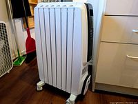 Side view of white oil-filled radiator showing vertical heating fins and wheeled base.