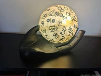 Lit plastic globe with black Sanskrit characters resting in carved wood hand base seen from front-left