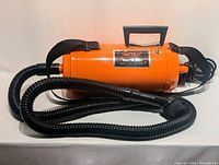 Orange Metrovac Vac-N-Blo portable canister vacuum with attached black hose and carrying handle, shown side view.