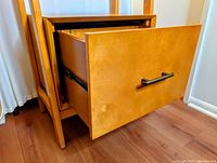Close-up of the drawer open showing blond wood finish and metal drawer slides with black rectangular handle.