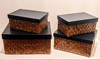 Four palm leaf boxes with woven texture and black leather-like lids, two large and two smaller boxes arranged in pairs.