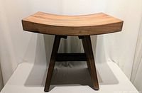 Front view of a teak wood bathroom stool showing seat curvature and four angled legs with stretcher support.