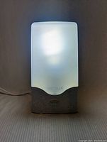 Front view of the Verilux light therapy lamp turned on, showing bright, diffused illumination from the frosted panel with brand logos visible on the base.