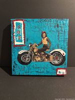 Square 12x12 mixed media collage artwork showing a teal textured background with a woman on a vintage motorcycle and the word 'dot' vertically on left.