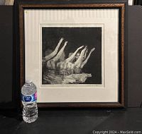 Framed etching with a water bottle for size reference, showing black and white image of ballerina in multiple poses extending arms.