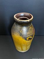 Front view of a yellowy brown glazed stoneware crock with a rounded rim and tapered body showing glaze blending and texture.