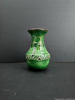 Front view of the small green ceramic vase with decorative banded design on a dark background.