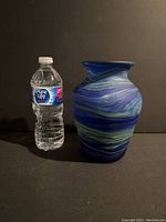 Front view of the blue and green swirled glass vase with water bottle for size comparison