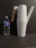 Front view of white metal jug with wooden handle and water bottle for scale.
