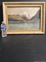 Framed mountain landscape print with three peaks, water and hills, alongside a water bottle for size reference.