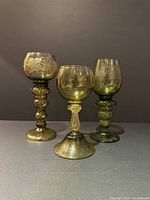 Front and side view of three green etched Hock glasses with different stem designs against black background.