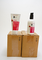 Two cardboard boxes each topped with one exfoliating sugar scrub tube and one body lotion bottle, showing packaging and containers.