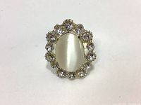 Top view showing the oval white center stone surrounded by clear rhinestones on silver-tone ring base.