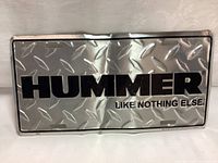Front view of metal HUMMER license plate with diamond plate pattern and slogan 'LIKE NOTHING ELSE'.