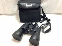 Front view of Bushnell Powerview binoculars with carrying case in background and neck strap showing.