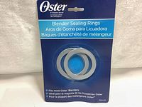 Front of packaging showing two gray circular blender sealing rings on a blue and white Oster branded cardboard.