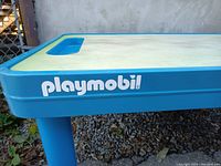 Close-up of Playmobil logo on table side showing blue plastic frame and white logo.