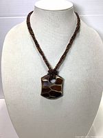 Front view of tortoise shell pendant necklace with giraffe pattern on a beige mannequin bust.