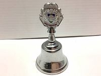 Full view of the silver-tone metal hand bell with the Antigua coat of arms on the handle