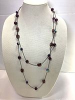 Full length of long necklace shown on white bust, showing bead types and placement.