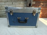 Front view of heavy duty flight case, blue with metal corner protectors and black handle, two metal clasps.