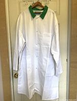 White long-sleeve lap or butcher coat with green collar hanging on hanger, front view showing full length and pocket.