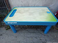 Front angle view of the rectangular Playmobil play table showing blue frame, legs, and textured tabletop surface with handle slot.