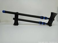 Folded carbon fiber camera crane jib arm showing blue adjustment rings and mounting plates.