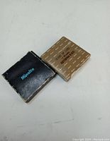 Two vintage Minolta branded boxes for close-up lens filters, one black and one brown with model info, placed on white surface.