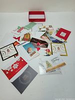 Assorted Christmas greeting cards spread out with different holiday images and messages visible, along with envelopes and red box.