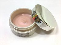 Open jar showing light pink cream inside with shiny silver lid beside it.